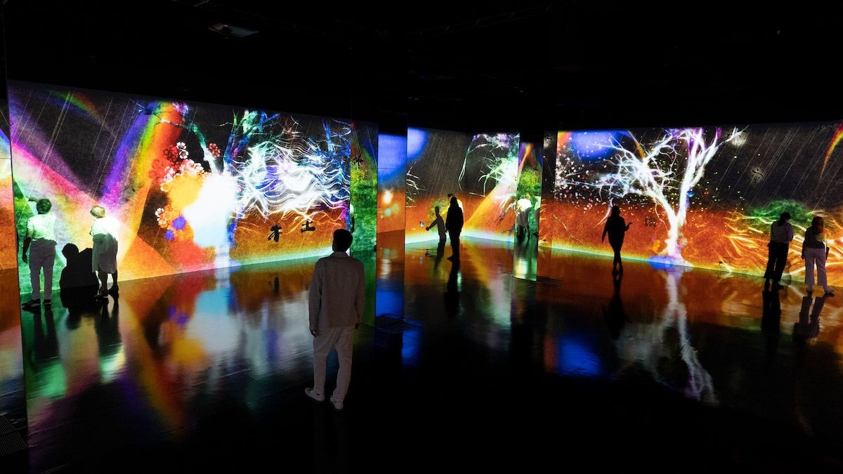 People observing colorful digital art projections on intersecting walls in a dark room.