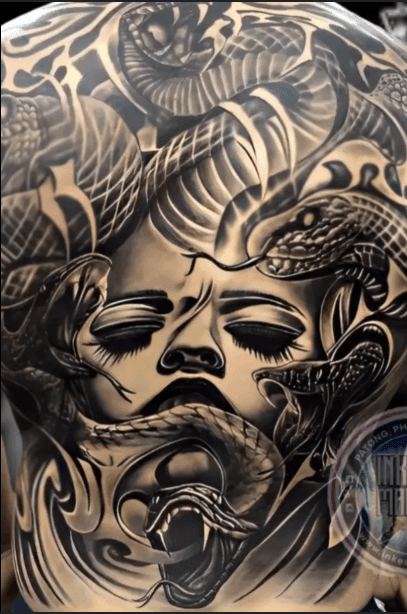 Intricate tattoo of a face surrounded by snakes and abstract patterns in black ink.