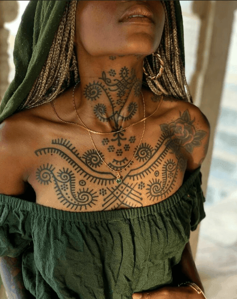 Person wearing a green outfit with intricate black tattoos on neck and chest.