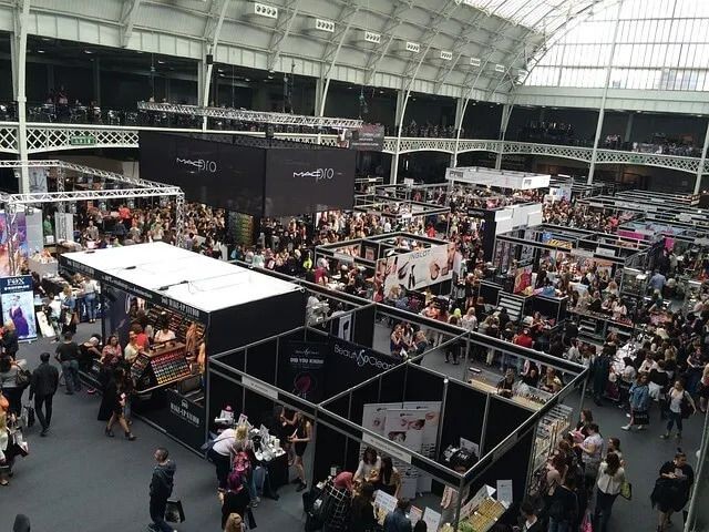 Crowded trade show with numerous exhibition booths and attendees in a large indoor venue.