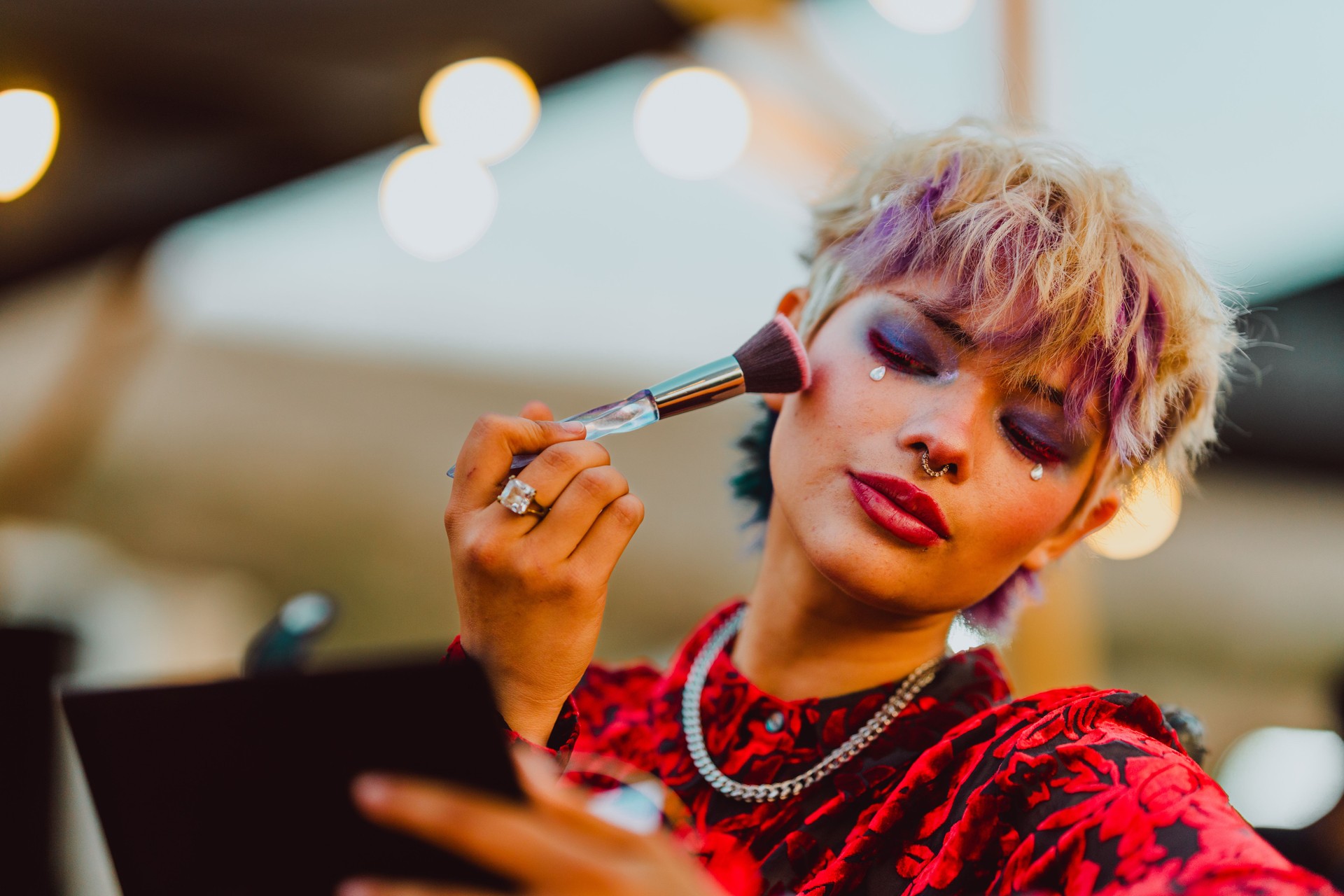 Stylish woman applying blush with a makeup brush outdoors.