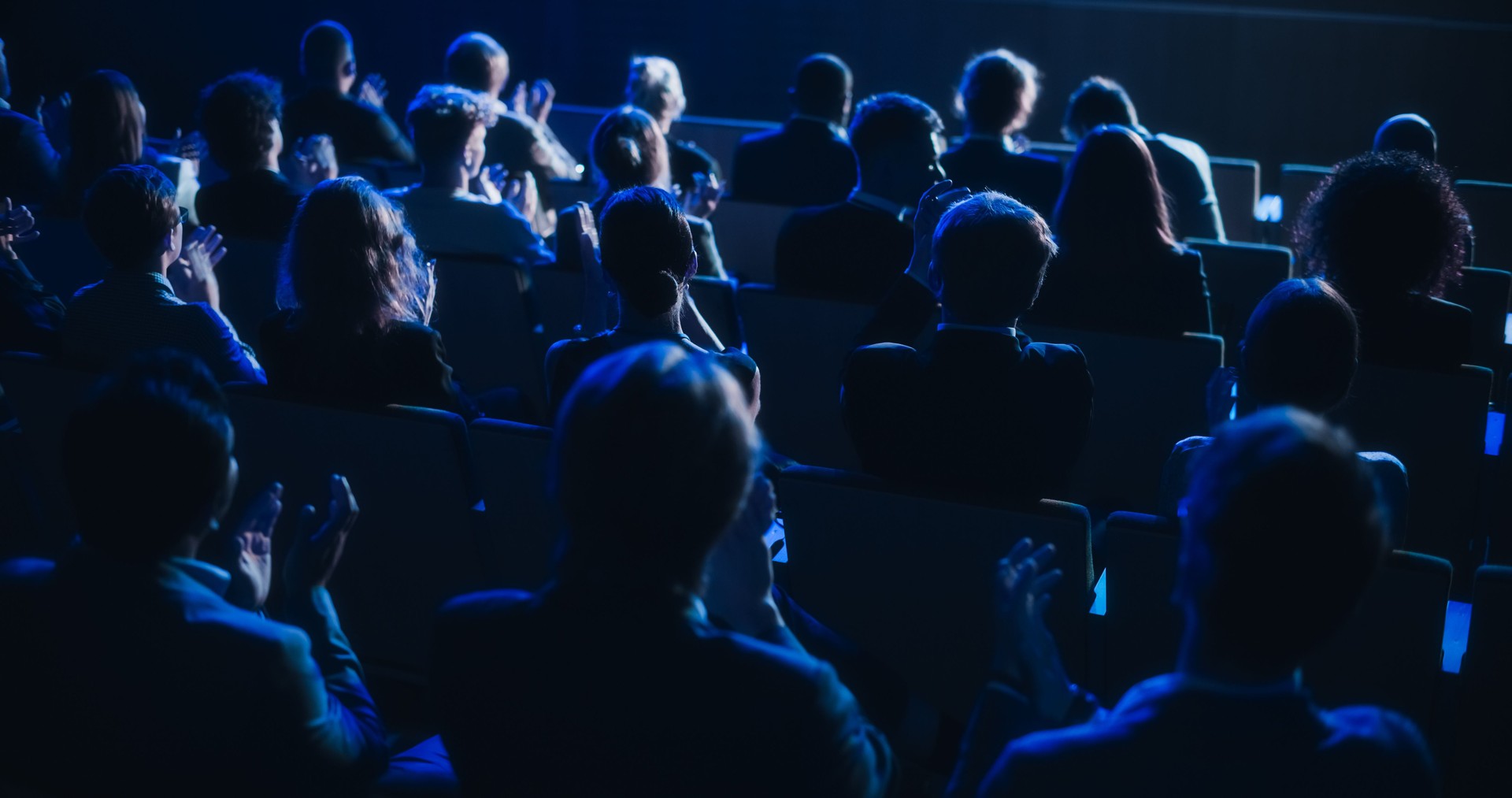 Crowd of Smart Tech People Applauding in Dark Conference Hall During a Motivational Keynote Presentation. Business Technology Summit Auditorium Room Full of Delegates. Footage from Behind.